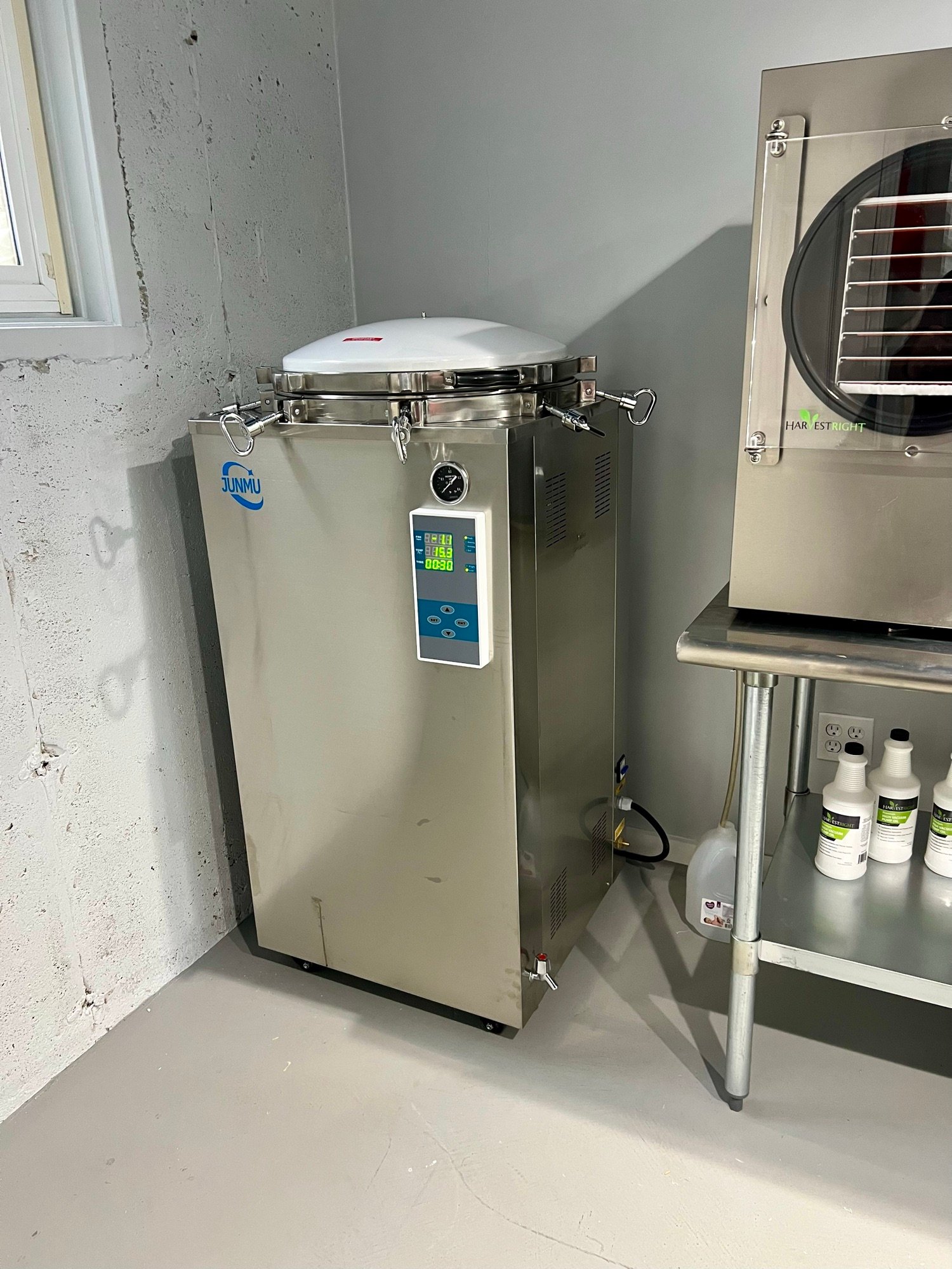 Industrial vertical autoclave alongside a Harvest Right freeze dryer in a clean room.