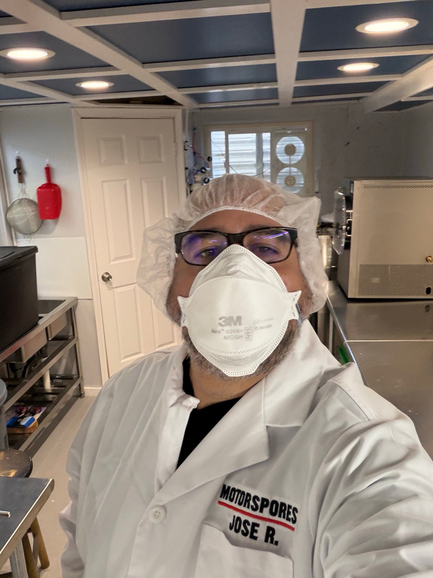 Jose Rivera in a MotorSpores lab coat, hairnet, and N95 mask, photographed in the lab.
